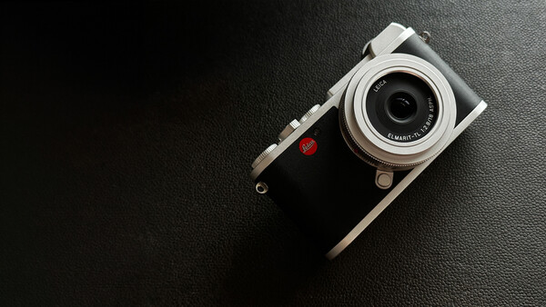 Rangefinder camera with silver top plate and black leather body on dark textured surface.