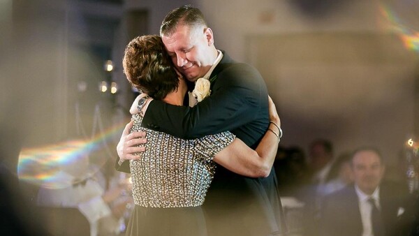 Couple embracing during a formal dance, with soft bokeh lighting and an indoor venue setting.