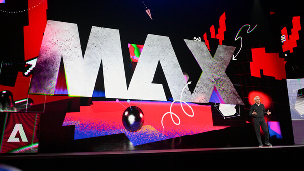 Large-scale conference stage display with bold MAX typography and vibrant neon pink and blue lighting effects.