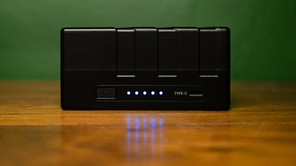 Black USB hub with five glowing blue LED indicator lights mounted on wooden surface against green background.