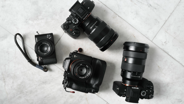 Collection of four black cameras and lenses arranged on a marble surface.