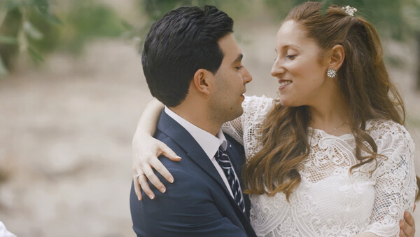 Bride and groom embrace outdoors, bride wearing lace wedding dress and groom in dark suit with striped tie.