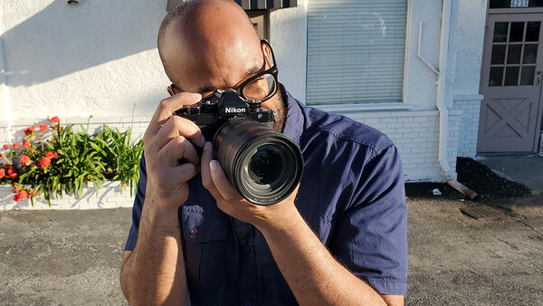 Photographer holding a Nikon DSLR camera with telephoto lens in bright outdoor sunlight.