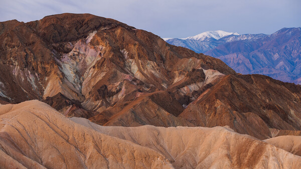 Layered desert mountains with warm earth tones, snow-capped peaks visible in the distance.