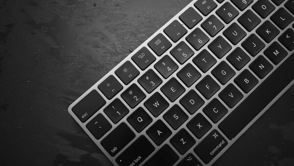 Overhead view of a silver and black wireless keyboard on a dark textured surface.