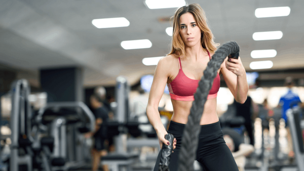 Woman in gym holding battle rope with focused expression during workout.