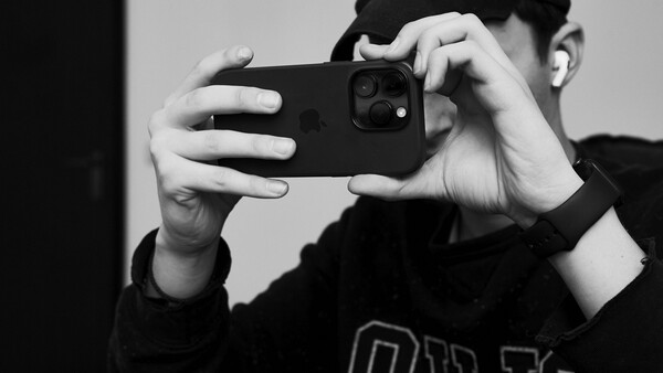 Person in black clothing holding smartphone horizontally to capture a photo, shot in black and white.