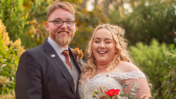 Bride and groom smiling outdoors during golden hour with lush greenery in the background.