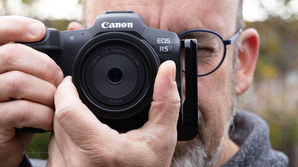 Man holding a Canon EOS R5 mirrorless camera with an RF 35mm lens attached.