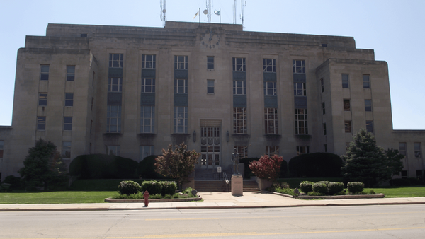 Symmetrical Art Deco government building with tan stone facade, central clock tower, and manicured landscaping.