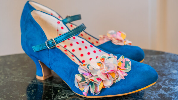 Pair of blue suede Mary Jane heels with colorful floral embellishments and red polka-dot lining.