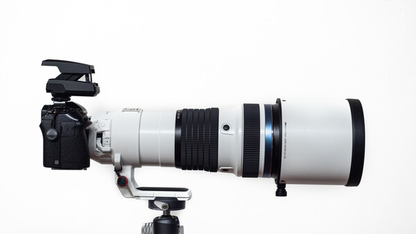 Professional telephoto lens with white barrel mounted on camera body with tripod collar and microphone attachment.