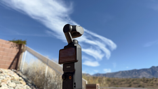 DJI Osmo Pocket gimbal camera mounted on a fence post overlooking desert landscape under blue sky.