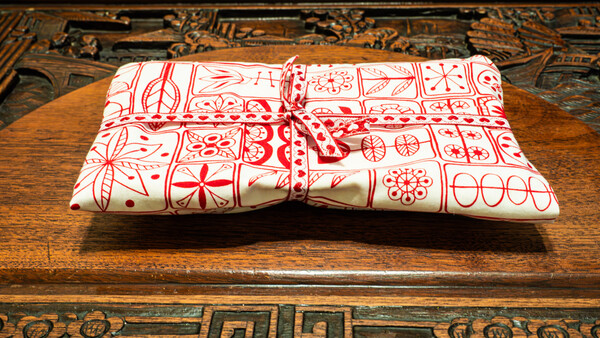 Red and white patterned fabric gift wrapped with twine bow on wooden table with ornate carved border.