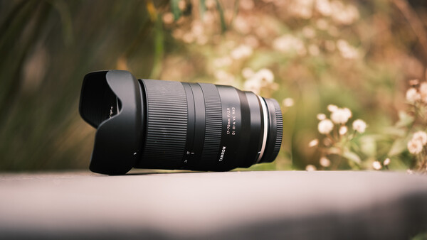 Black telephoto lens with hood mounted on neutral surface against blurred garden background.