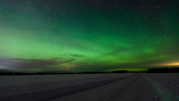 Aurora borealis illuminates the night sky in brilliant green above a frozen landscape and dirt road.