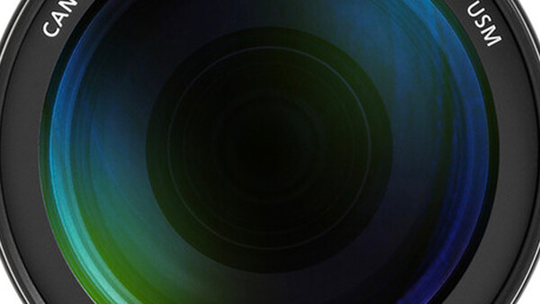Close-up view of a camera lens barrel showing multicoated glass elements with blue and green light reflections.