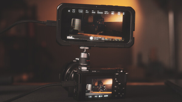 Cinema camera and external monitor mounted on tripod displaying warm-toned footage in dimly lit studio.