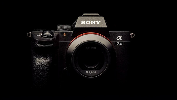 Sony a7 III mirrorless camera body with FE 2.8/35 lens mounted, photographed against black background.