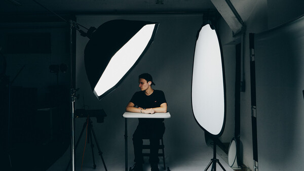 Photographer seated at desk in studio with two large oval softbox lights positioned on either side.