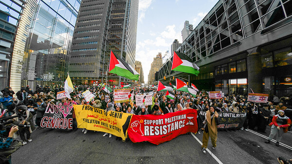 Large protest march filling a city street with Palestinian flags and demonstrators holding signs.