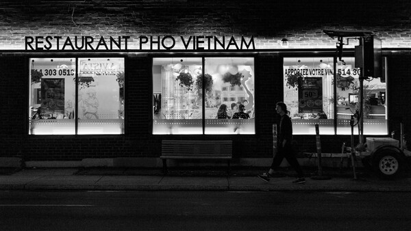 Black and white storefront of a Vietnamese pho restaurant with three large display windows and illuminated signage at night.