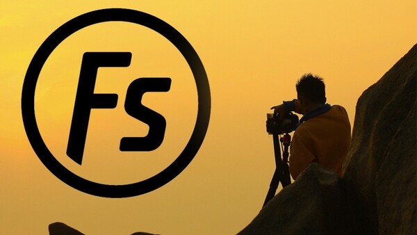 Silhouetted photographer operating a camera on a rocky outcrop against a golden yellow sky with the Fstoppers logo.