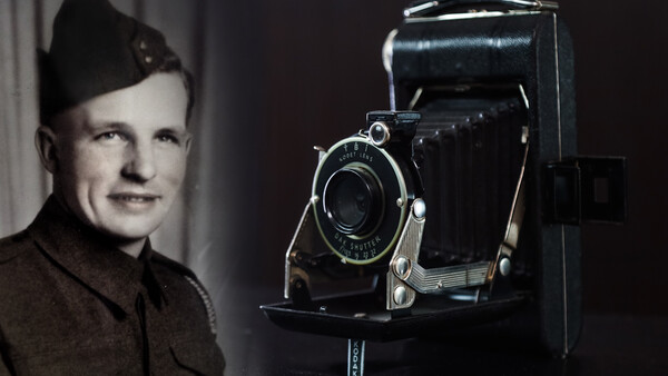 Man in military uniform posing beside a large format folding camera on a stand.