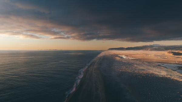 Aerial view of a sandy coastal spit extending into dark ocean waters at dusk.