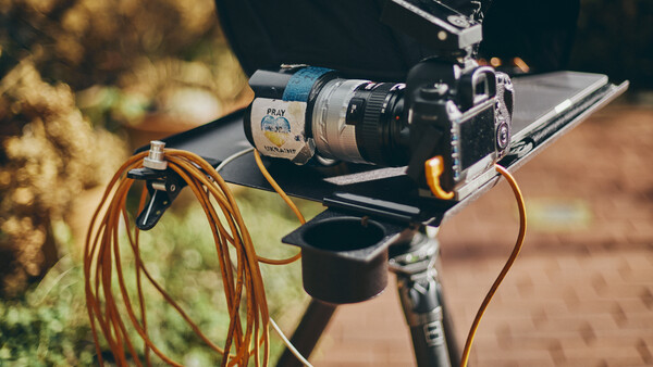 Film camera mounted on a rig with coiled orange cables and external audio equipment attached.