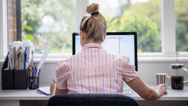 Person working at desk with laptop, viewed from behind, natural window light streaming across workspace.