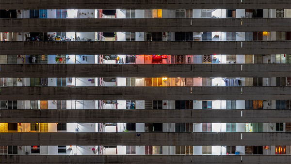 Apartment building facade at night showing illuminated windows across multiple floors with varied interior lighting and decor.