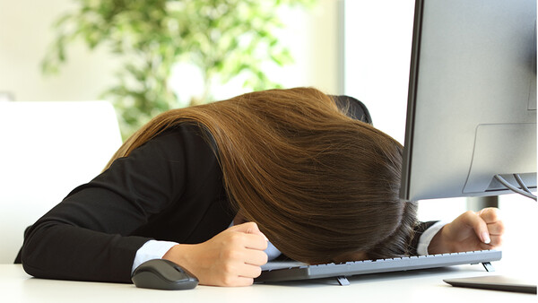 Person in black blazer slumped over desk with head resting on keyboard.