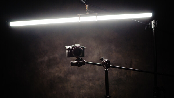 Camera mounted on a boom arm under a bright LED panel light against a textured brown backdrop.