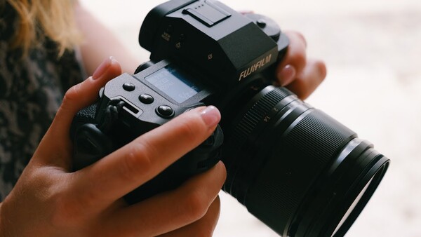 Hands holding a mirrorless camera with attached telephoto lens and external flash unit.