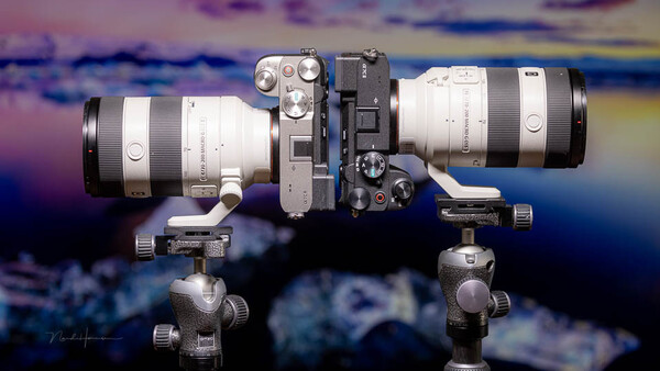 Two telephoto lenses mounted on ball head tripod mounts against colorful sky backdrop.