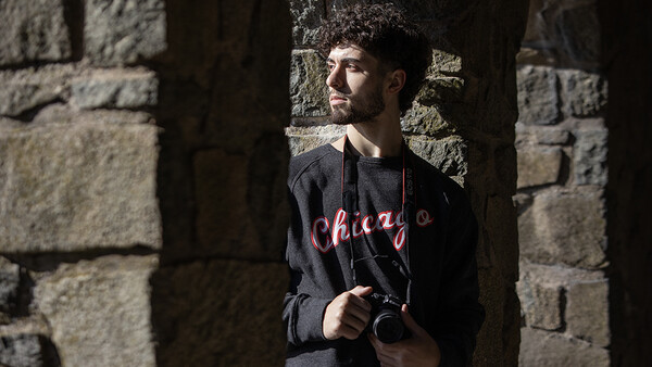 Man holding a camera while standing in shadow between stone walls.