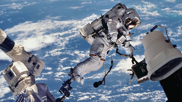 Astronaut performing a spacewalk with Earth and clouds visible in the background.