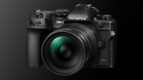 Olympus OM-1 mirrorless camera with attached lens, photographed against a dark gray background.
