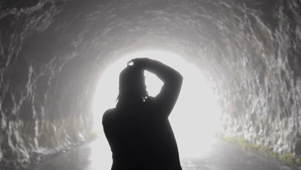 Silhouetted figure standing in a tunnel looking toward bright light at the end.