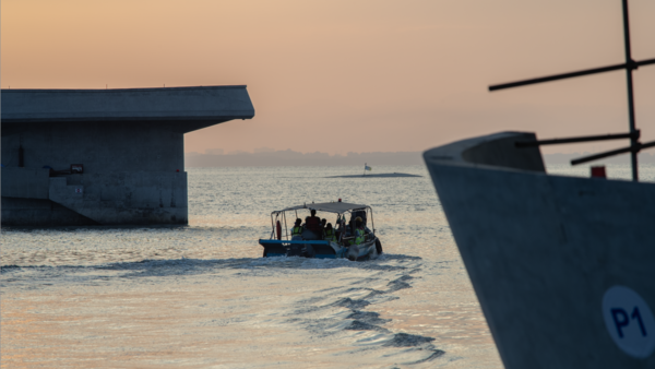 Small fishing boat navigating shallow water between moored vessels at golden hour.