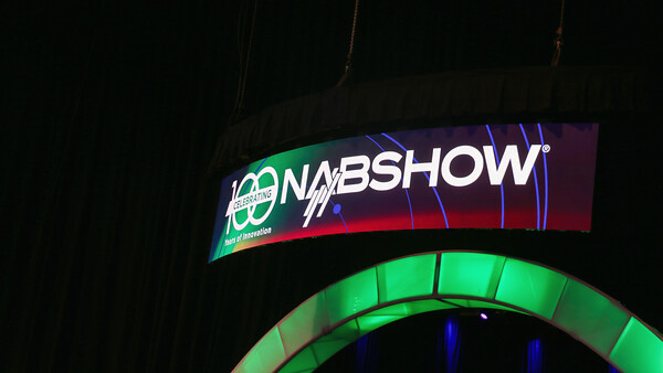 Illuminated NAB Show signage with curved green and red neon lighting against dark background.