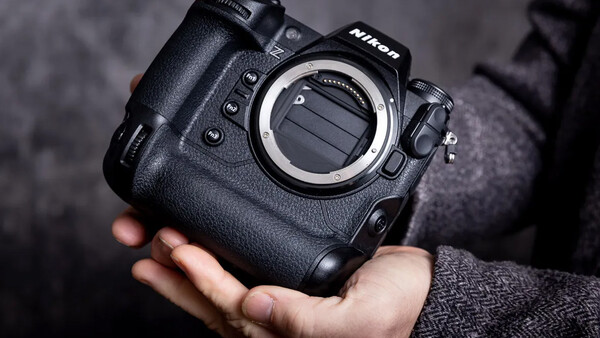 Nikon professional camera body held in hands, showing the lens mount and control buttons against a dark textured background.