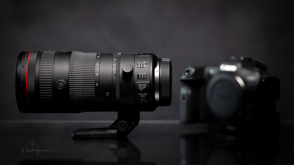 Professional telephoto lens with red ring mounted on stand, camera body blurred in background.