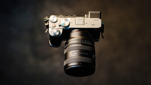 Overhead view of a silver mirrorless camera with attached zoom lens on dark background.