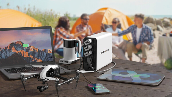 Photography and camping gear arranged on a wooden table with tents and campers visible in the background.