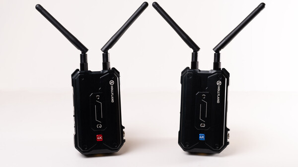 Two black wireless transmission units with dual antennas positioned side by side against a white background.