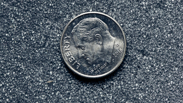 Close-up of a silver coin with a profile portrait facing left on a textured gray surface.