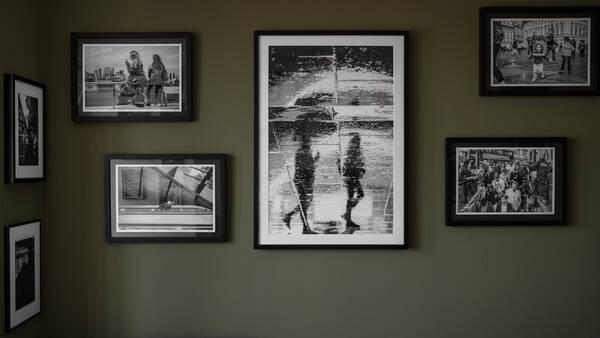 Gallery wall with seven black-framed black and white photographs arranged on olive-green wall.