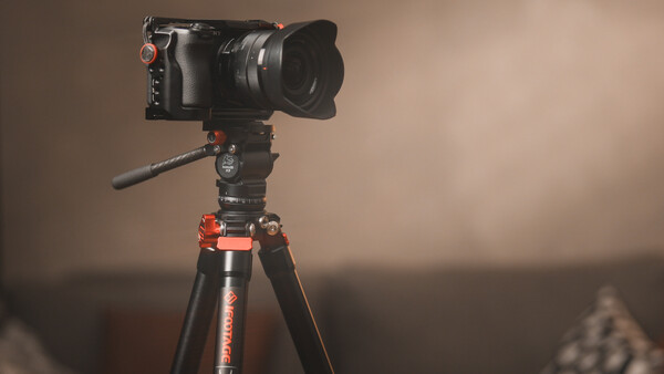 Professional cinema camera mounted on tripod with fluid head and extended lens hood.